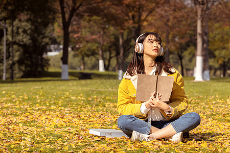 金色耳机坐在满地银杏叶下听音乐的女孩背景