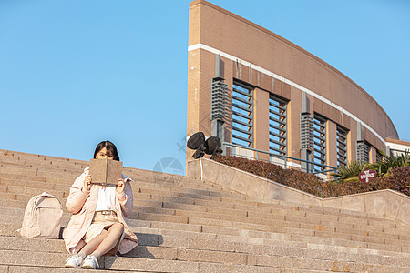 坐在台阶上手拿书本的女大学生图片