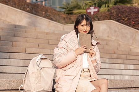 坐在台阶上手拿书本的女大学生图片