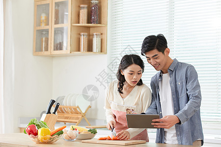 年轻夫妻拿着平板电脑学习做菜图片