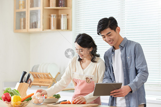 年轻夫妻拿着平板电脑学习做菜图片