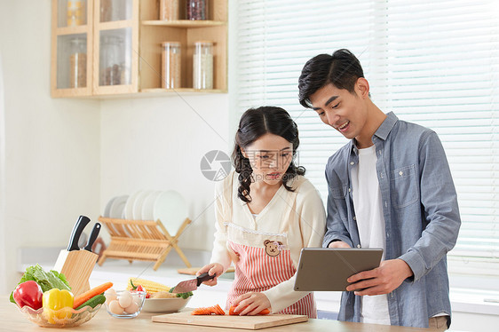 年轻夫妻拿着平板电脑学习做菜图片