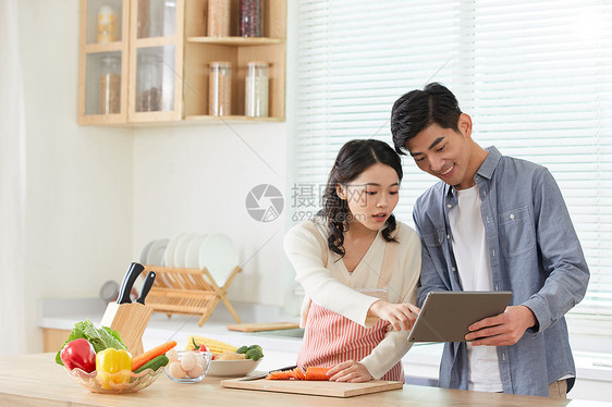 年轻夫妻拿着平板电脑学习做菜图片