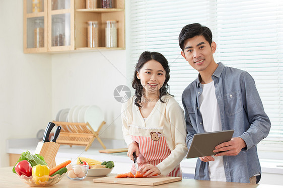 年轻夫妻拿着平板电脑学习做菜图片