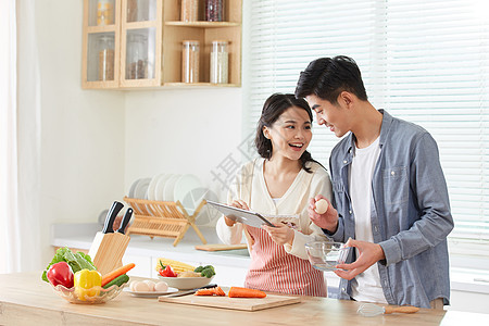 年轻夫妻拿着平板电脑学习做菜图片