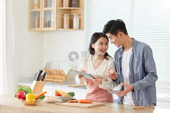 年轻夫妻拿着平板电脑学习做菜图片