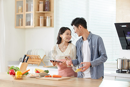 年轻夫妻拿着平板电脑学习做菜图片