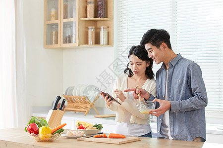 年轻夫妻拿着平板电脑学习做菜图片