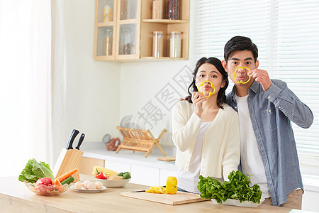 年轻情侣在厨房拿黄辣椒片卖萌背景图片
