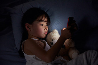 小女孩躺在床上玩手机图片