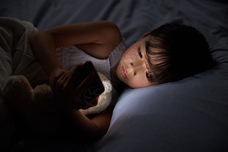 夜晚看书小女孩躺在床上玩手机背景