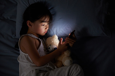 小女孩躺在床上玩手机背景图片