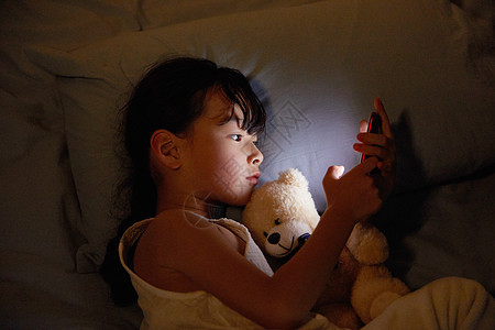 小女孩夜晚躺床上玩手机图片