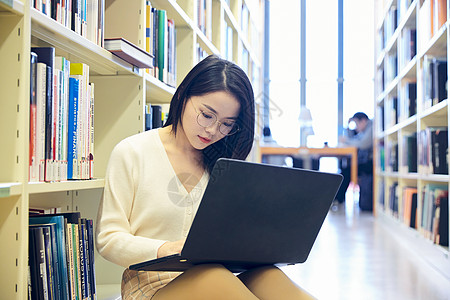 在图书馆看书年轻女士在图书馆用笔记本电脑学习背景