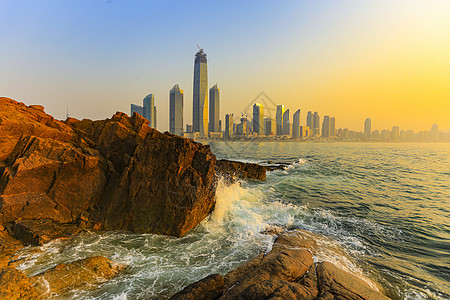 剪影日出时的海浪礁石和城市高楼背景