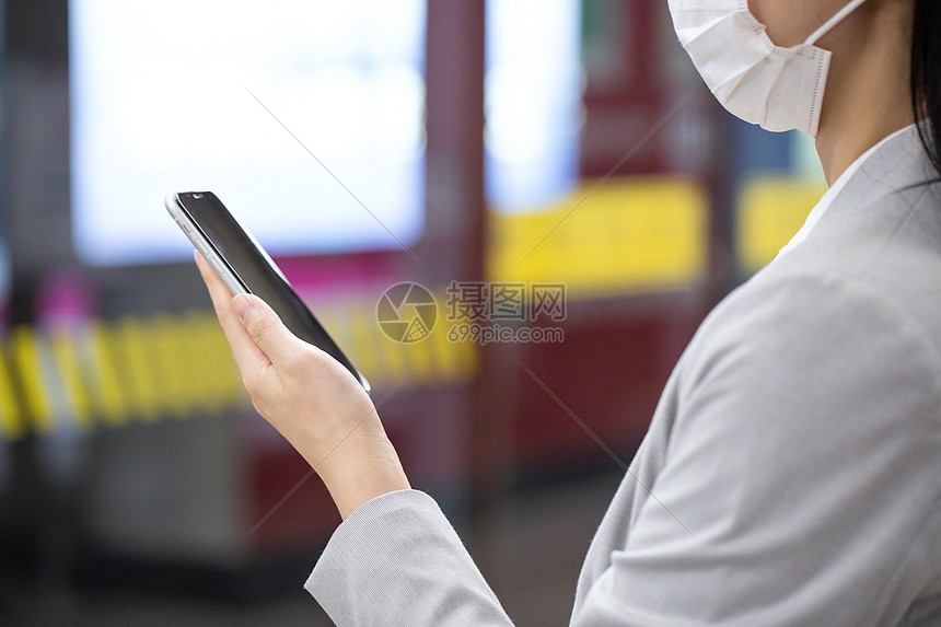 女性戴口罩拿手机乘地铁等候图片