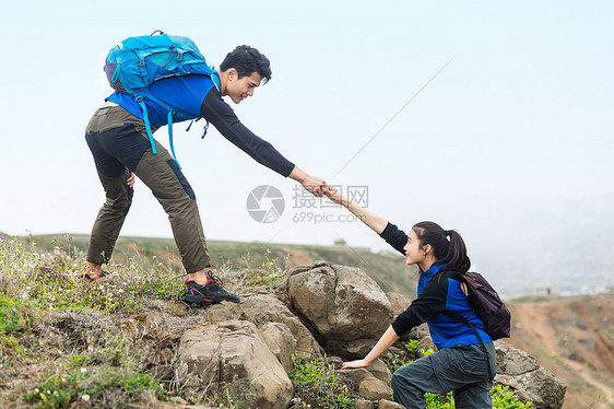 郊外合作携手爬山的男女青年图片