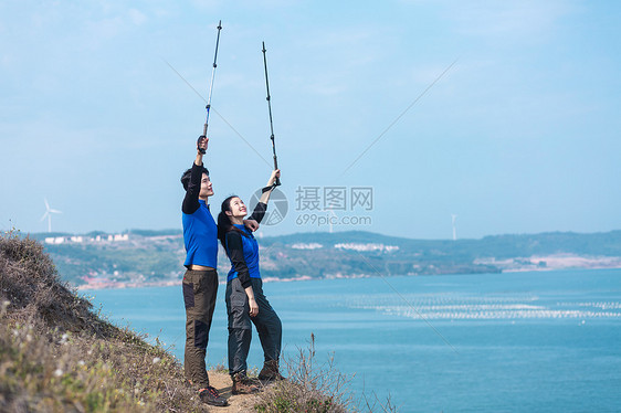 海边山坡上举登山杖男女图片