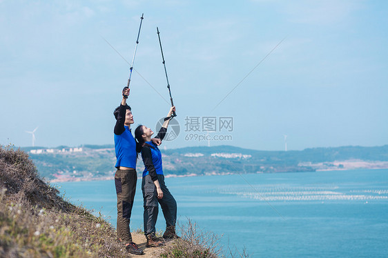 户外站在海边举登山杖的情侣图片