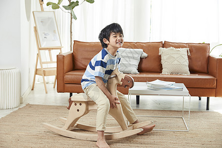 小男孩在客厅玩木马玩具图片