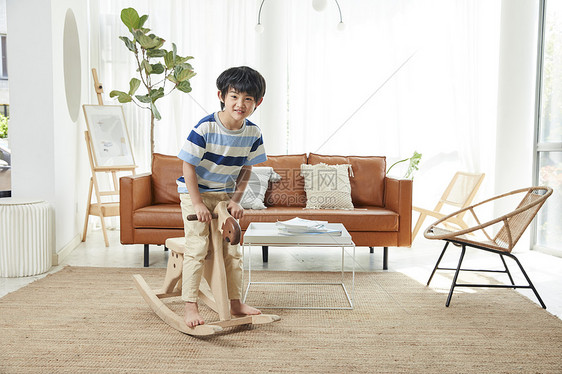 小男孩在客厅玩木马玩具图片