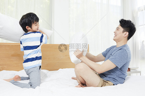 年轻爸爸和孩子在床上枕头大战图片