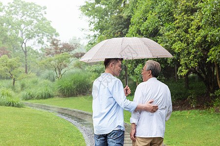 中老年父子撑伞下雨天逛公园图片