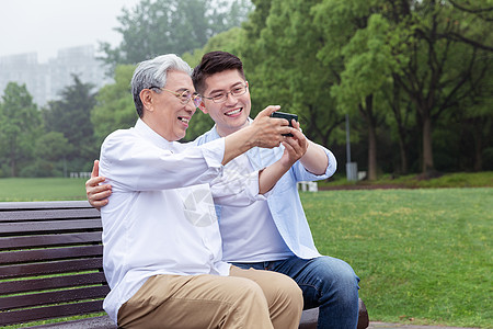 中老年父子公园长椅上手机自拍图片