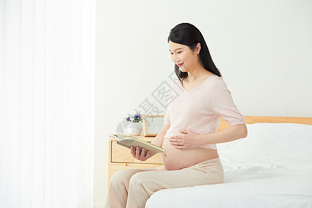 孕妇坐在床边阅读背景图片