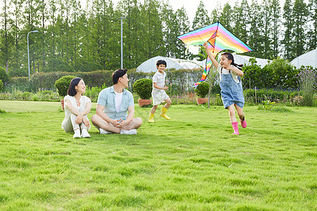 开心生活年轻夫妻看着孩子追逐玩风筝背景