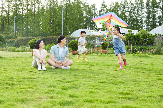 年轻夫妻看着孩子追逐玩风筝图片