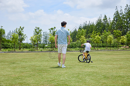 爸爸陪伴小男孩骑自行车背影图片