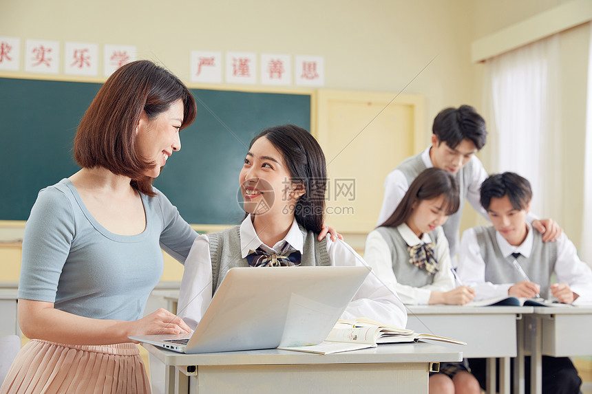 女教师使用笔记本电脑给学生辅导图片