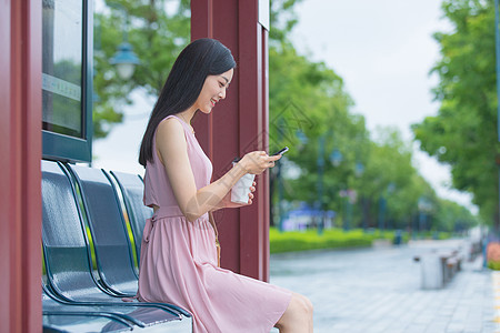 坐在公交站台玩手机的女性背景图片