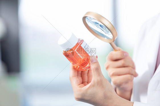 女性医疗科研人员拿放大镜观察新研制药品图片