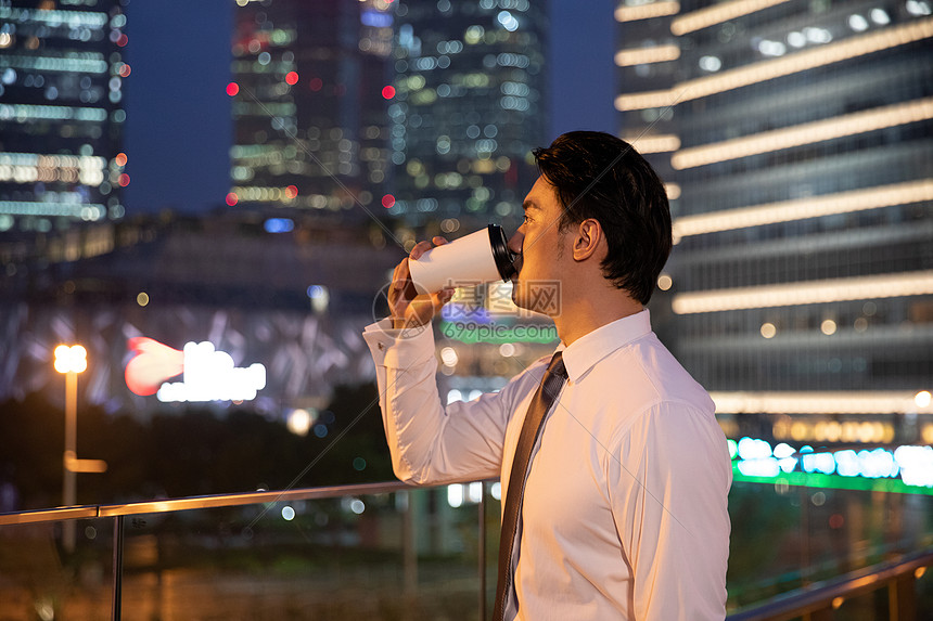 夜晚天桥上的都市商务男性喝咖啡图片