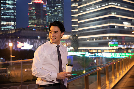 夜晚天桥上的都市商务男性手捧咖啡图片