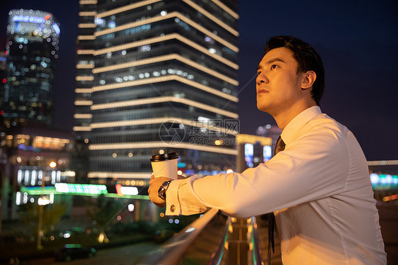 夜晚都市天桥上的商务男性手捧咖啡图片