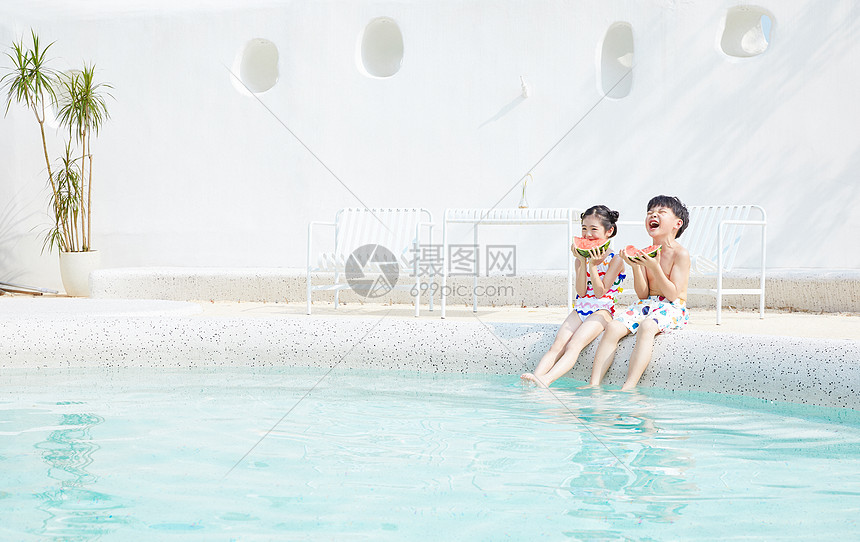 夏天小男孩和小女孩坐在泳池边开心吃西瓜图片