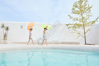 男孩女孩拿着游泳圈在泳池边行走图片