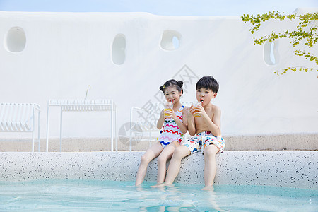 小男孩和小女孩坐在泳池边喝果汁图片