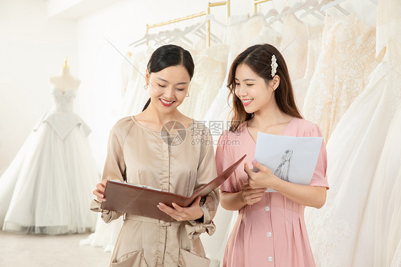 服装设计师手拿设计稿为顾客定制婚纱图片