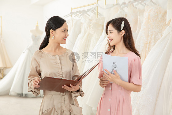 服装设计师手拿设计稿为顾客定制婚纱图片