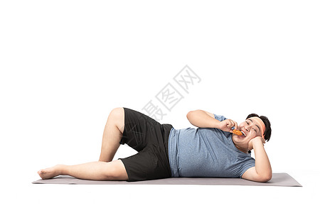 肥胖男生躺在瑜伽垫上吃零食图片