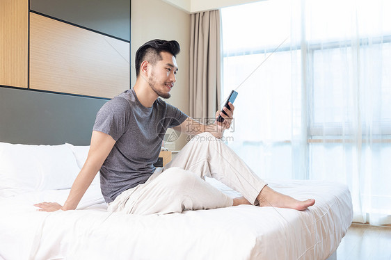 商务男性躺在酒店床上看手机图片