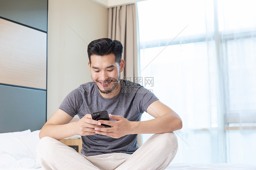 青年男性坐在酒店床上看手机图片