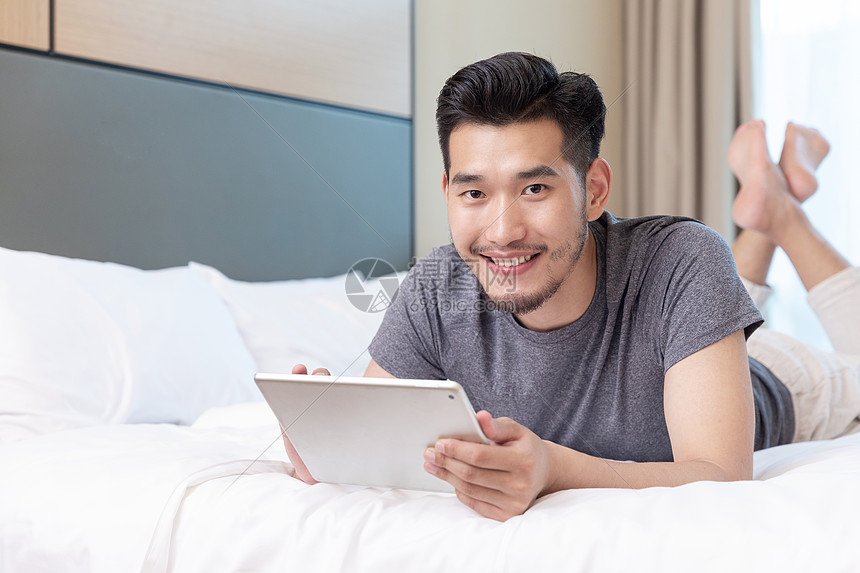 商务男性趴在酒店床上玩平板电脑