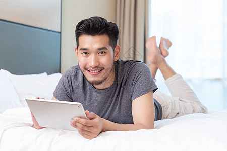 商务男性趴在酒店床上玩平板电脑图片