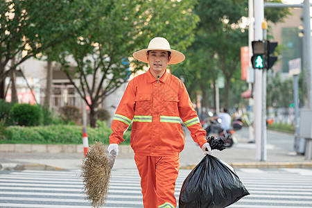 拎着垃圾袋与扫帚的环卫工人过马路图片