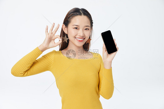 穿黄色毛衣拿着手机比OK手势的美女图片